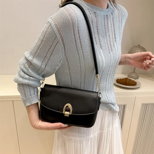 Classic black crossbody bag with gold horseshoe buckle worn with a light blue knit sweater