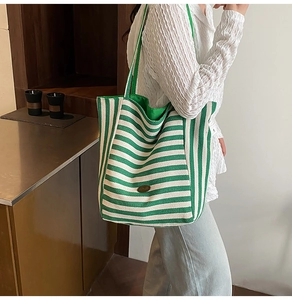 Detail of green and white striped canvas tote bag featuring an oval metal logo plaque