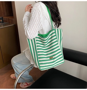 Detail of green and white striped canvas tote bag with woven shoulder strap on model