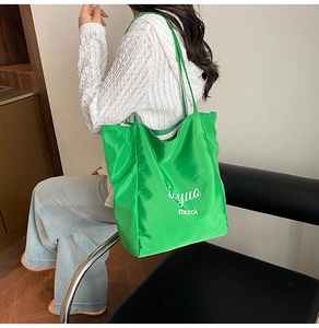 Close-up of vibrant green canvas tote bag with white letter print on a model shoulder