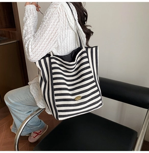 Detail view of black and white striped canvas tote bag featuring handmade oval metal plaque