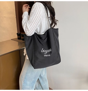 Detail of a large black canvas tote bag with white letter print and durable shoulder straps