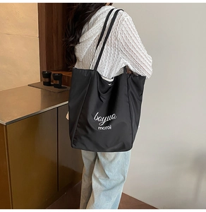 Detail of a large black canvas tote bag with white lettering on model's shoulder