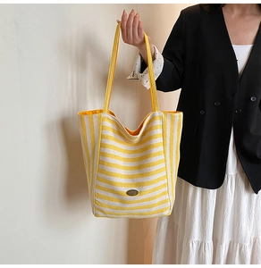 Detail of yellow striped canvas tote with oval metal logo plate on the front