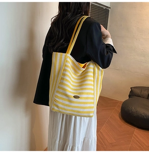 Side view of large yellow and white striped canvas tote bag on female shoulder