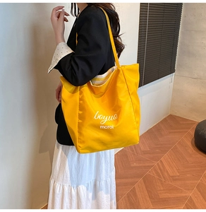 Detail of a bright yellow nylon tote bag featuring a white artistic text print on the front