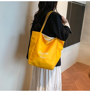 Detail of a bright yellow large canvas tote bag with white artistic lettering print