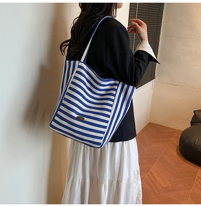 Detail of blue and white striped canvas tote bag with metal brand tag and spacious design