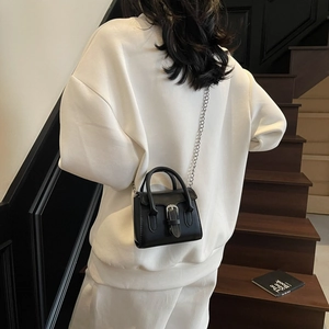 Mini black leather trapezoid handbag with silver buckle and chain on white casual outfit