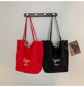 Detail of red and black canvas tote bags with contrast striped straps on a wooden hook