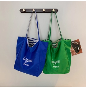 Close-up of nylon tote bags with striped webbing handles and printed graphic letters