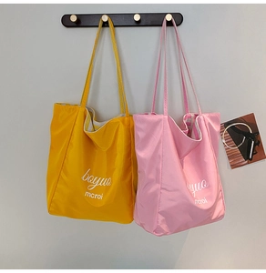 Detail of lightweight nylon tote bags in yellow and pink hanging on a black wooden hook
