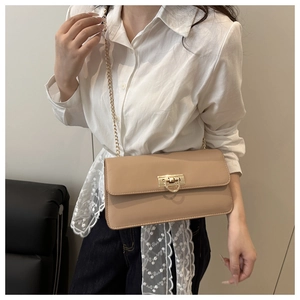 Detail of a beige leather crossbody bag featuring a gold clasp and metal chain strap