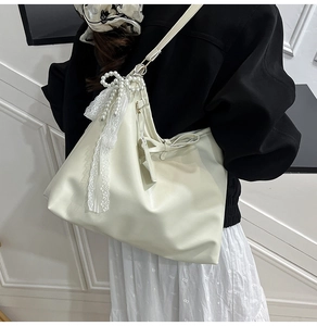 Détail d'un sac sous les bras blanc cassé avec nœud en perles et ruban de dentelle