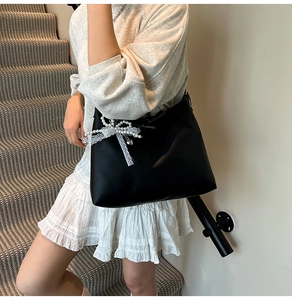 Detail of black matte shoulder bag with white lace and pearl bow charm accessory