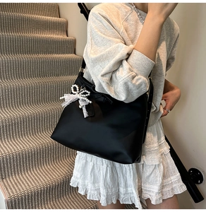 Détail d'un sac bandoulière noir avec un nœud en dentelle blanche et pendentif perle