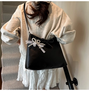 Detail of black faux leather tote with pearl bow and white lace decor on model