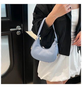 Detail of light blue crescent shoulder bag with lizard pattern texture on model arm