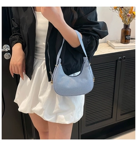 Close-up of a light blue denim crescent shoulder bag with elegant gold zipper hardware