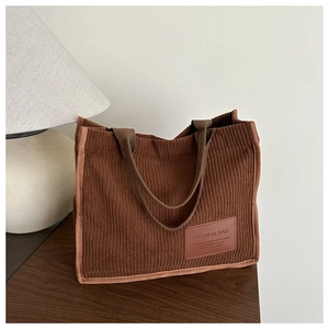 Detail of brown corduroy tote bag with dual handles and fashion leather patch detail