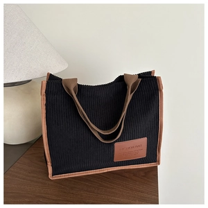 Detail of black corduroy tote bag with brown trim and leather fashion logo on a wooden desk