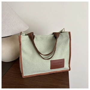 Detail of light green corduroy tote bag with brown leather tag on a wooden surface