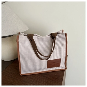 Detail of corduroy tote bag with brown leather label and reinforced stitching handles
