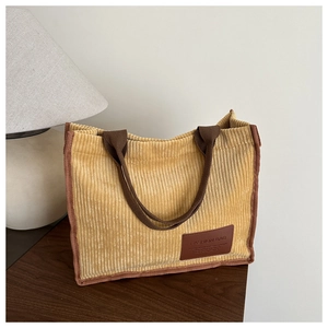 Detailed close-up of yellow corduroy tote bag with vertical texture and leather logo