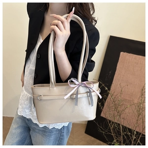 Detail of a cream faux leather tote bag with a decorative ribbon on a model side view