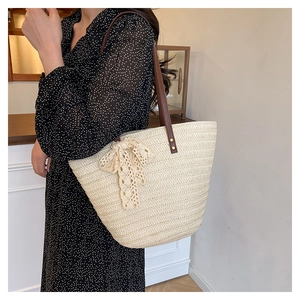 Detail of straw woven tote with cream lace bow and brown leather handles on shoulder
