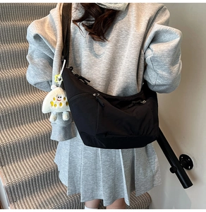 Detail of black nylon crescent bag with multiple pockets and cute plush charm on strap