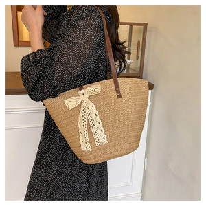 Detail of hand-woven straw tote bag with cream lace bow and premium brown leather handles