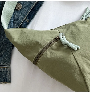 Close-up of green nylon crossbody bag featuring a zipper with a woven rope puller