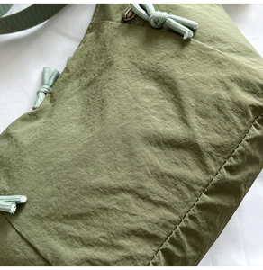 Detail of green nylon shoulder bag featuring side drawstring knot and visible stitching