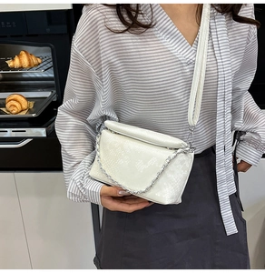 Detailed view of white snake-embossed crossbody bag with silver chain and thin leather strap