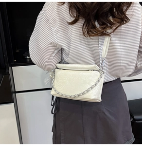 Detail of off-white snake-embossed crossbody bag with stylish silver metal chain strap