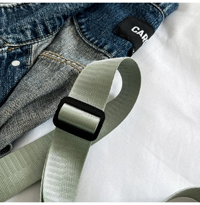 Detail of adjustable green nylon strap and black plastic buckle on a denim bag