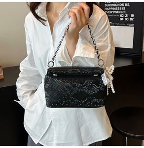 Detail of black snakeskin texture bag with silver chain, pearl and lace charms