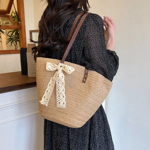 Handcrafted straw tote bag with cream lace bow and brown leather straps in a cafe setting