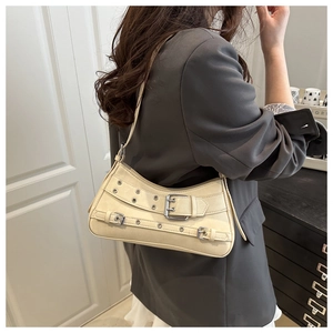 Close-up of beige rivet shoulder bag with metal eyelets and adjustable buckle straps
