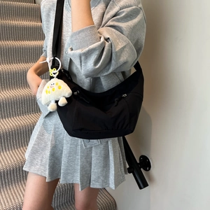 Minimalist black crescent crossbody bag with white mushroom pendant on a model