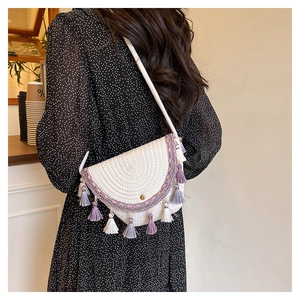Détail du sac tressé blanc avec broderie ethnique et pompons colorés porté à l'épaule