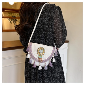 Detail of bohemian woven crossbody bag with purple embroidery and tassel accents on model