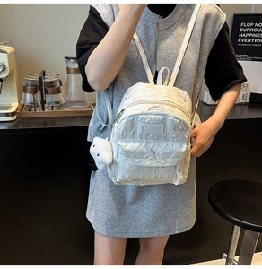 Detalle de mini mochila blanca con diseño de rombos, bordado y colgante de gato
