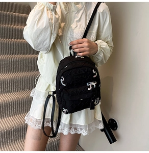 Detalle de mini mochila negra con bordado de lazo y placa metálica con el logo de marca