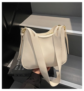 Detail of cream leather tote bag featuring a wide shoulder strap and gold metal buckle