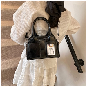 Gros plan du sac Boston en cuir verni noir avec fente pour carte sur une robe blanche