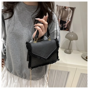 Détail d'un sac bandoulière noir mat avec bordures à franges et bandoulière dorée