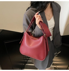 Side view of dark red soft leather hobo bag held by model wearing a grey suit