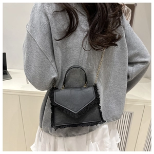 Model wearing a black tassel crossbody bag with golden chain strap and textured leather finish